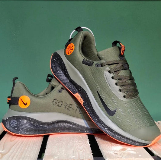 Green and black athletic shoes with orange accents on a wooden surface and green background