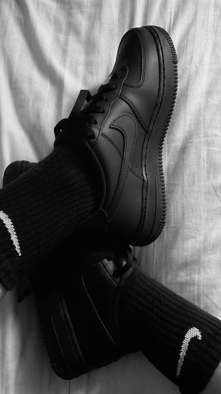 Black sneakers with a logo worn with black socks on a light fabric background