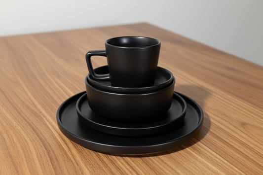 Set of black ceramic dishes including a cup, saucer, and plate on cardboard boxes.