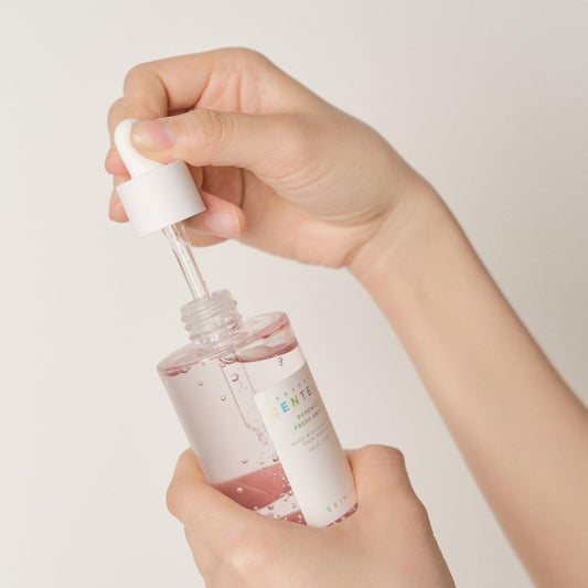 Hand holding a small dropper bottle with a white cap against a plain background