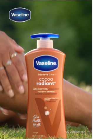 Vaseline Intensive Care Cocoa Radiant lotion bottle with a person applying it on their arm outdoors.