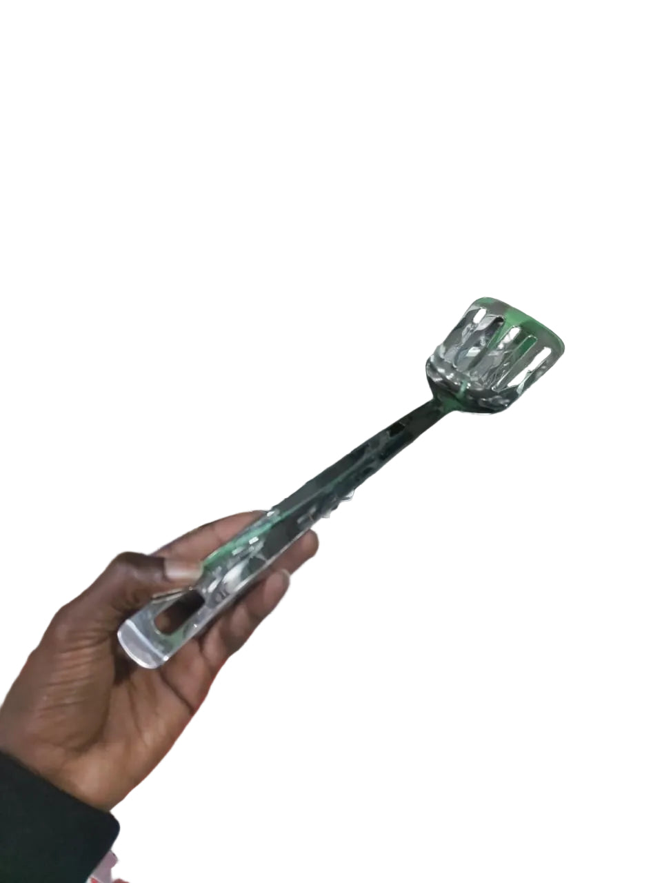 Metallic slotted spoon held by a hand in front of a cluttered storage area.