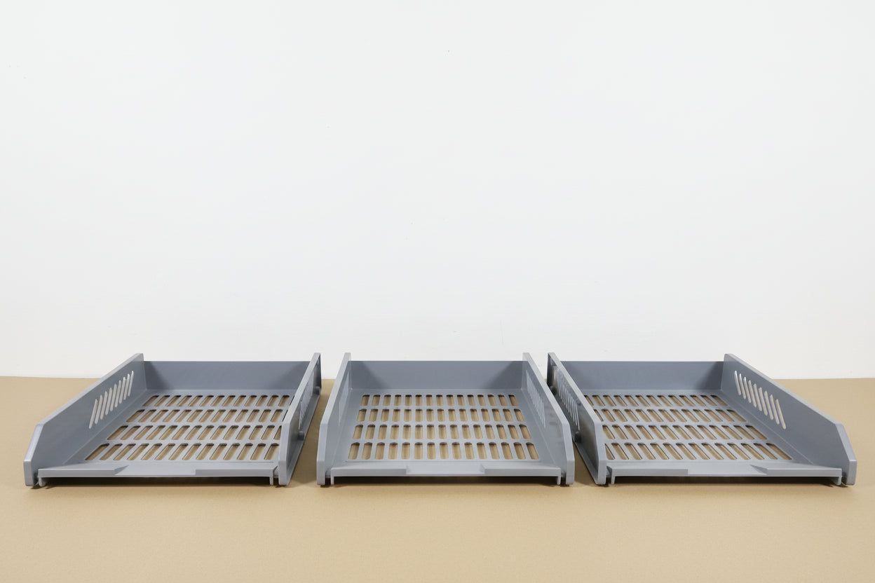 Three gray plastic drawers on a wooden surface with a white wall in the background.