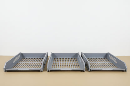 Three gray plastic drawers on a wooden surface with a white wall in the background.