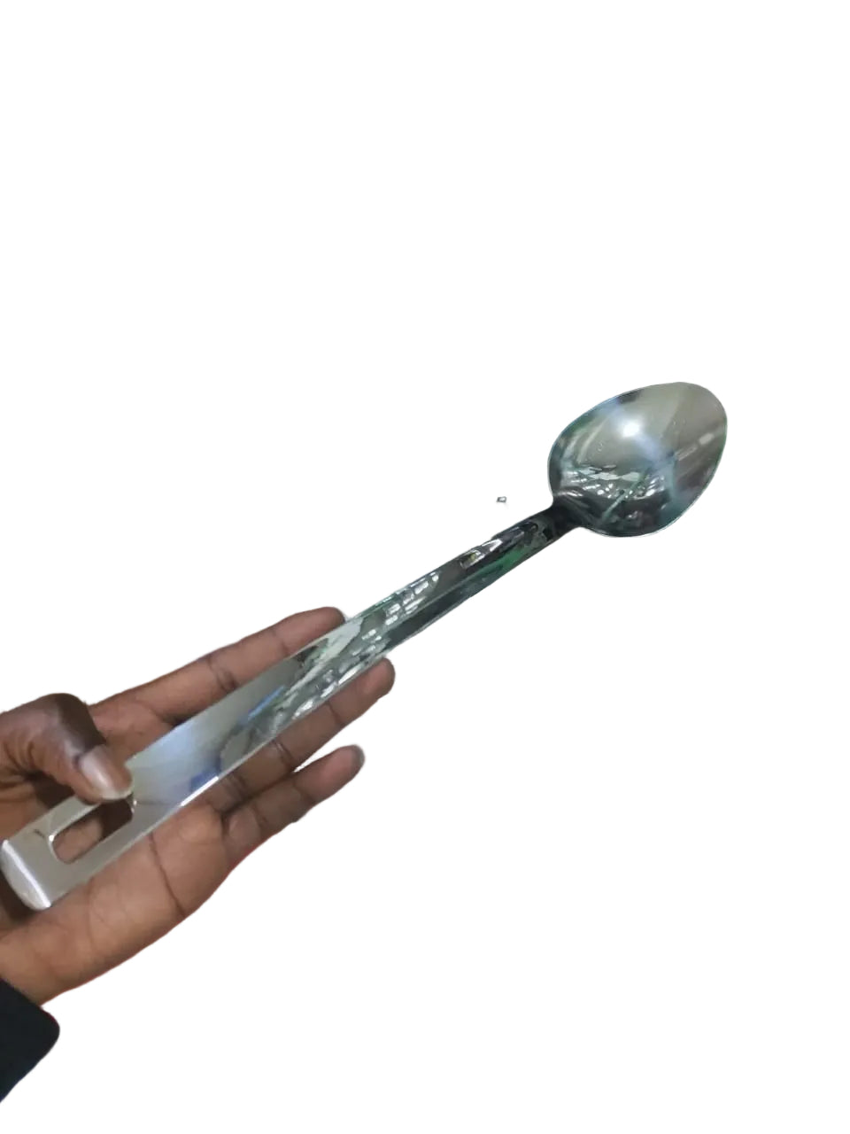 Person holding a large spoon in front of a cluttered background with shelves and various items.