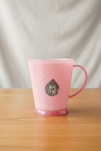 Pink mug with a brand logo held by a hand against a cluttered background