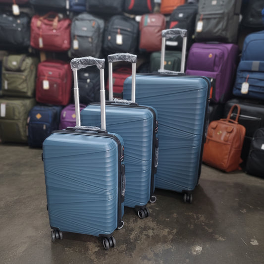 Three blue suitcases with clear plastic wrap on a concrete floor.