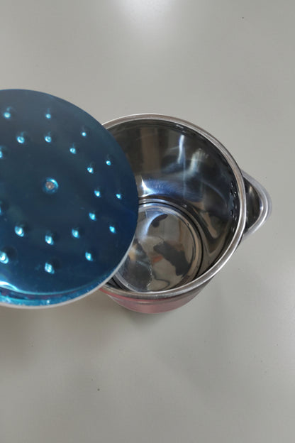 Stainless steel pot with blue lid on a concrete floor