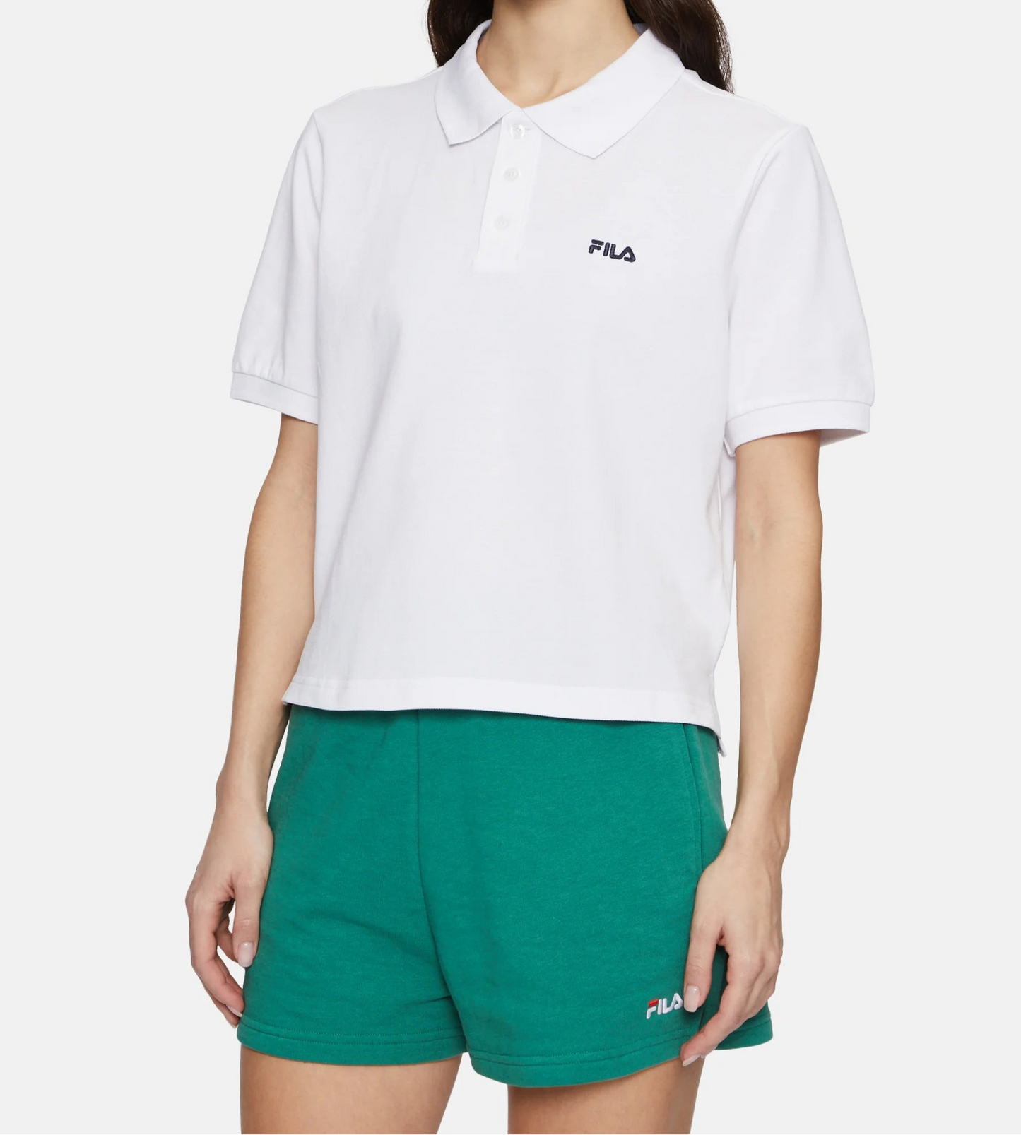 Woman wearing a white FILA polo shirt and green shorts on a white background