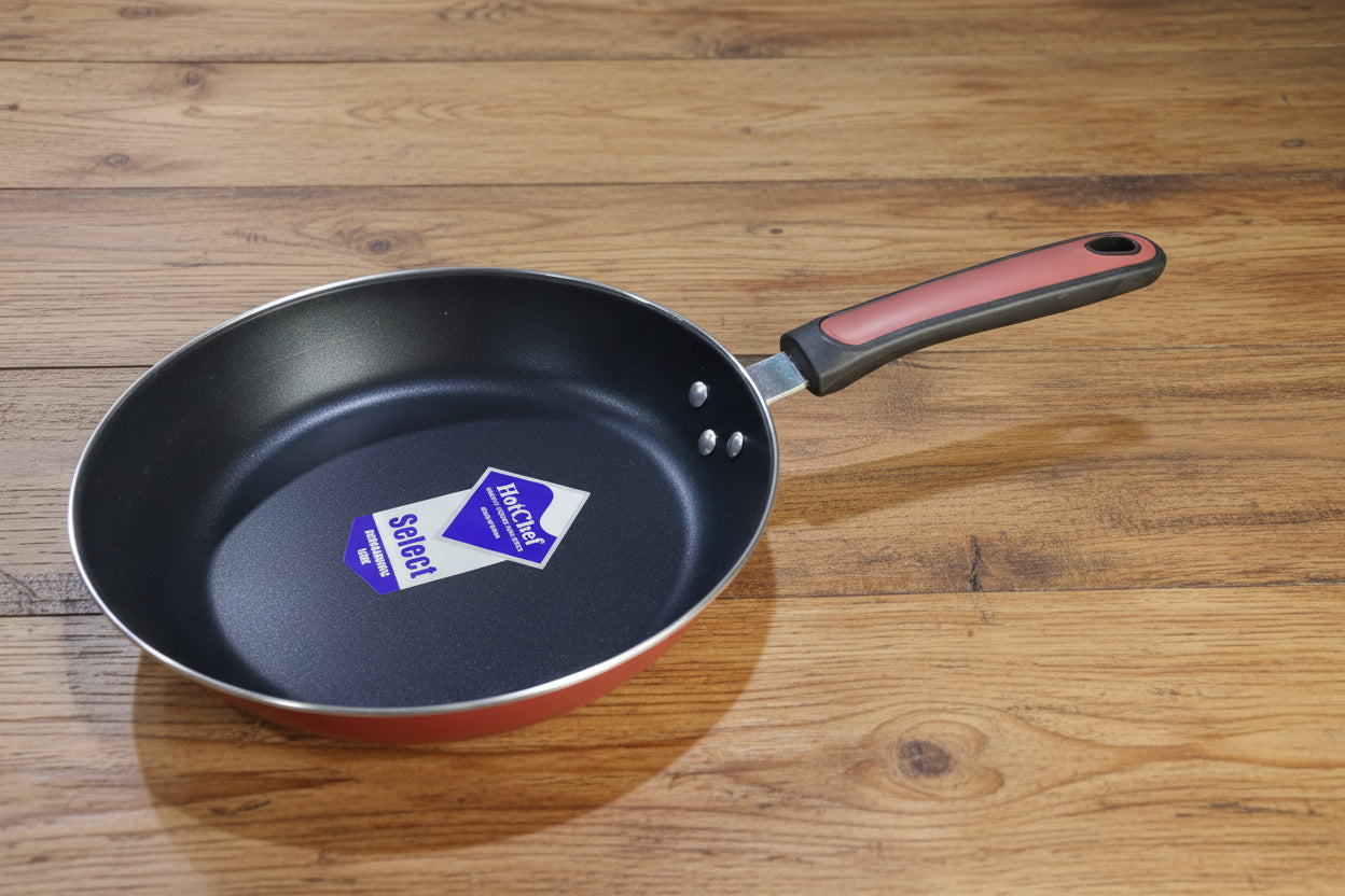 Black frying pan with a visible brand label on a cluttered background of kitchenware.