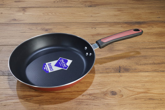 Black frying pan with a visible brand label on a cluttered background of kitchenware.