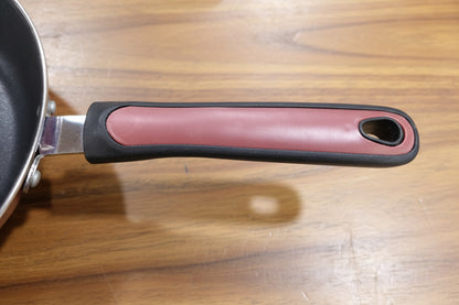 Frying pan with a red handle on a green surface