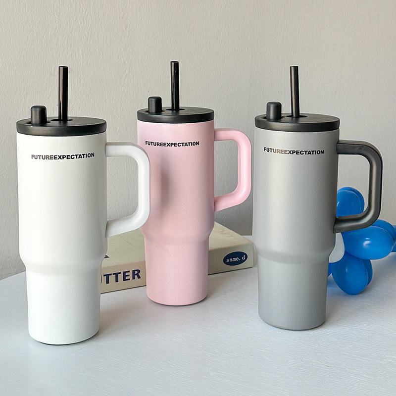 Three insulated travel mugs with handles and straws on a light surface.