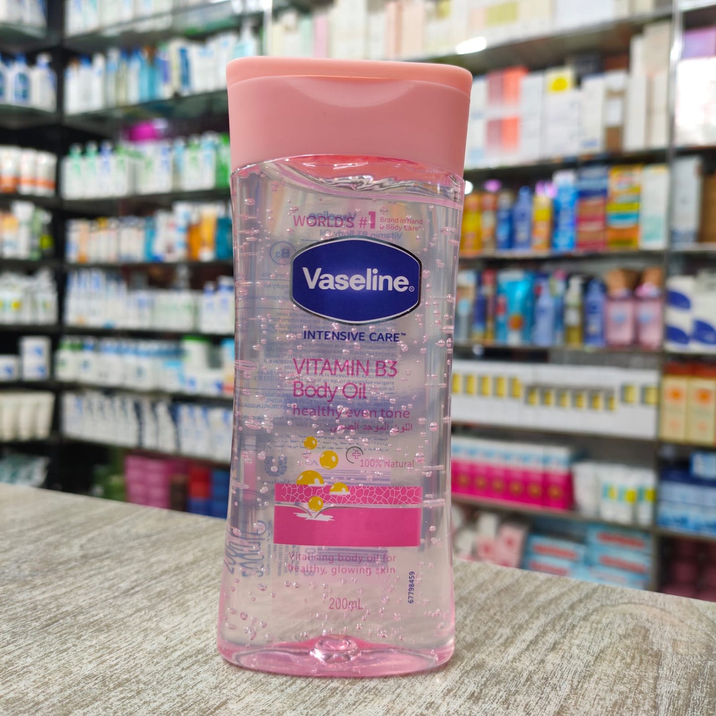 Vaseline Vitamin B3 body oil bottle with a pink cap on a shelf in a pharmacy.