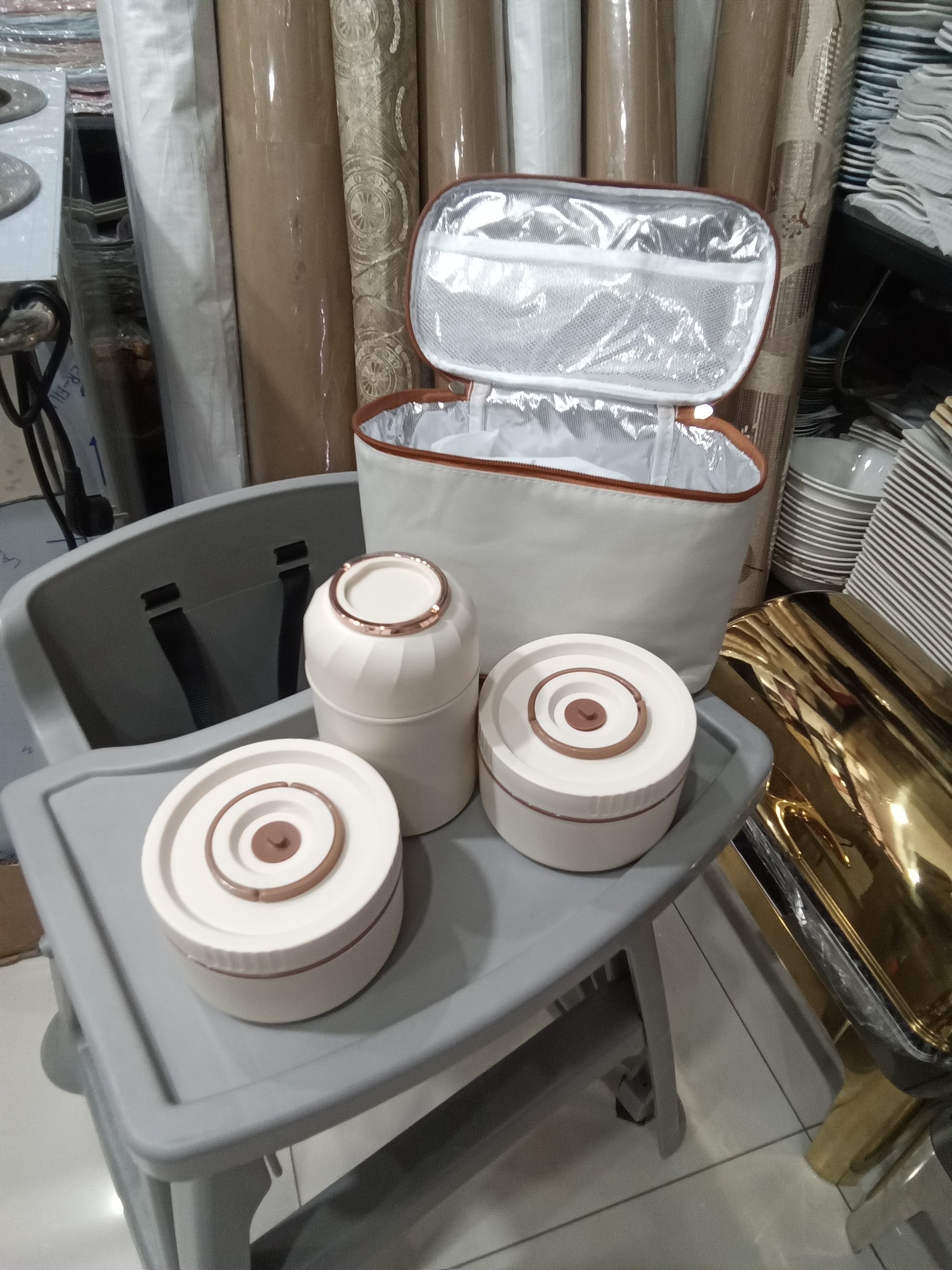 Set of white containers with brown patterns on a gray surface, with an open insulated bag in the background.