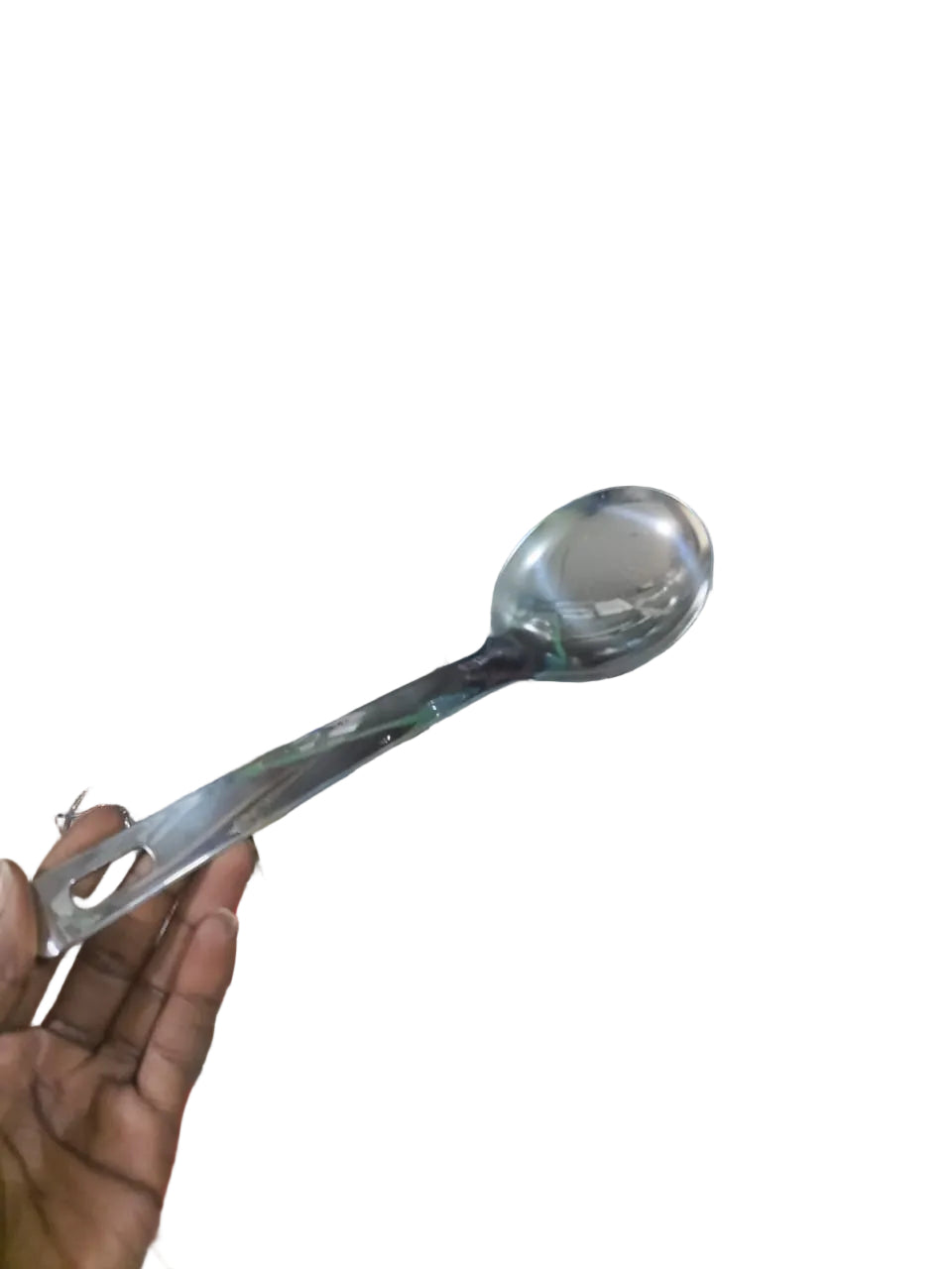 Person holding a silver spoon in front of a cluttered background with shelves and various items.