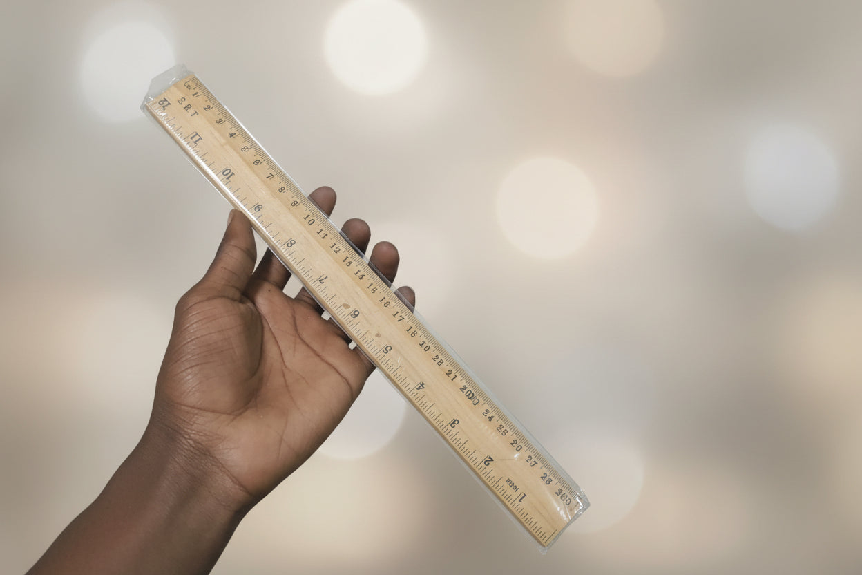 Hand holding a wooden ruler against a cluttered background