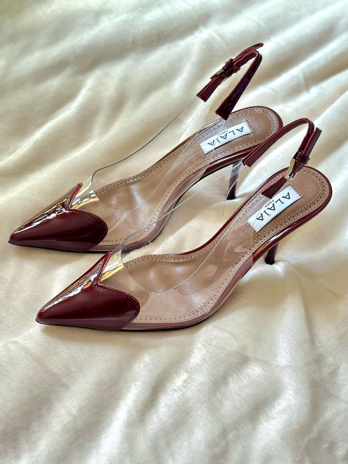 Pair of red high-heeled shoes with clear soles on a light fabric background