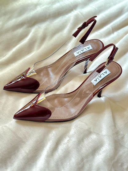 Pair of red high-heeled shoes with clear soles on a light fabric background