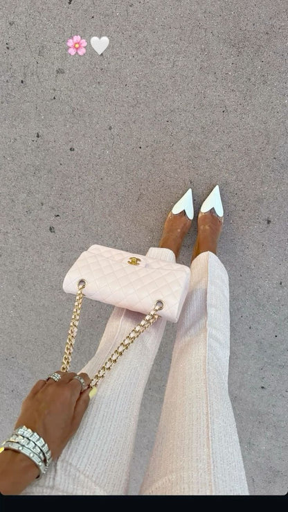 Person holding a small white handbag with gold chain on a gray pavement background