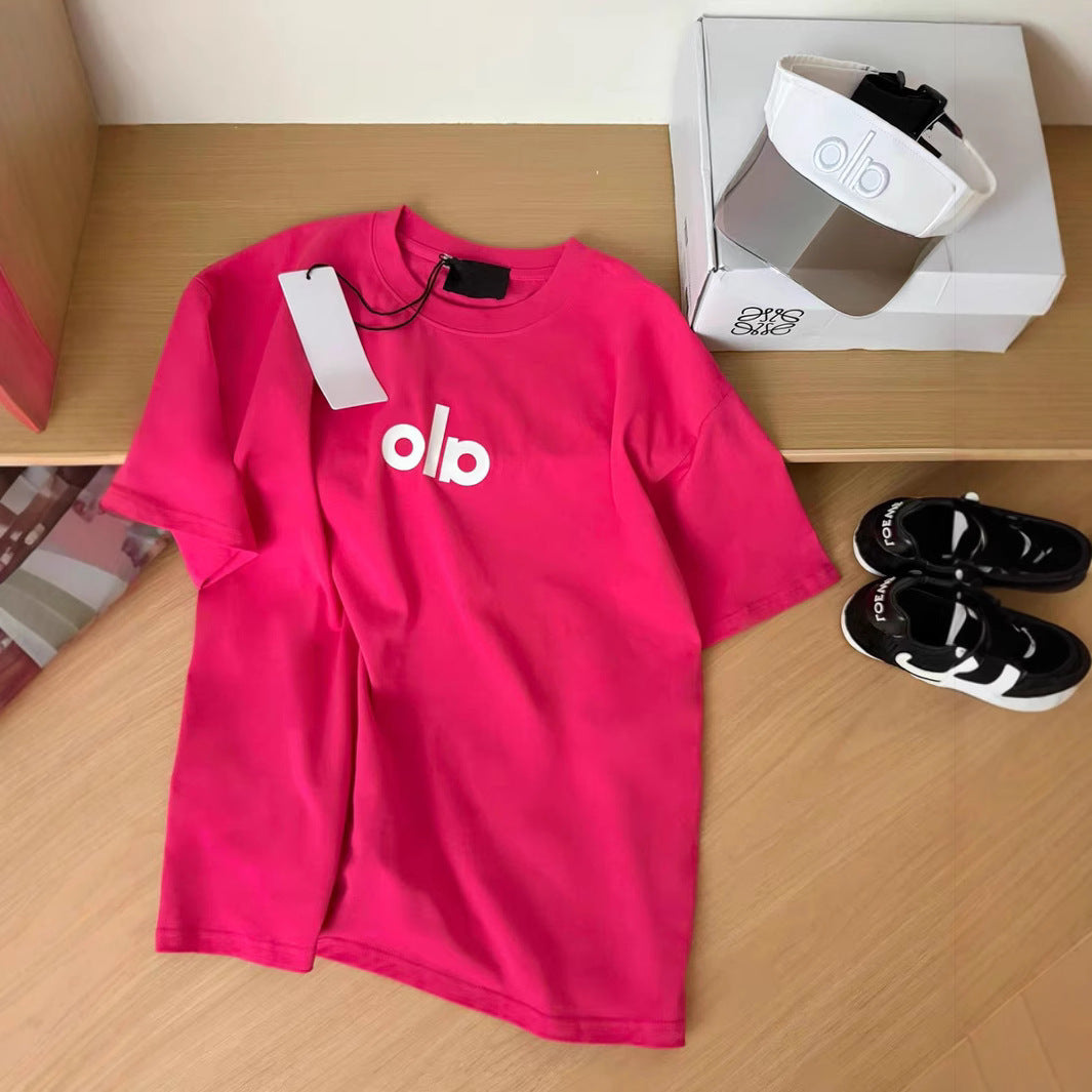 Pink t-shirt with 'olo' logo on a wooden surface, next to a white box and black shoes.