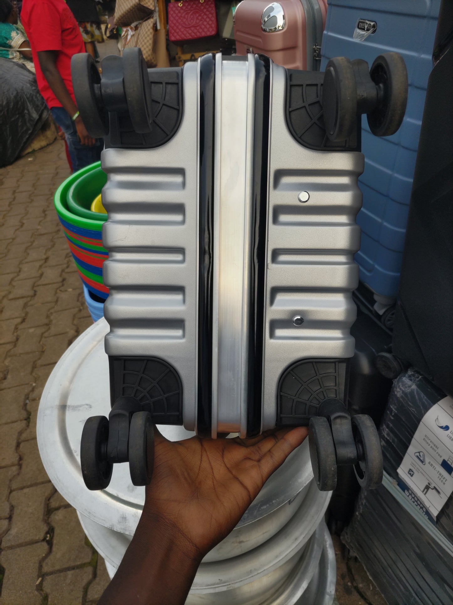 Silver suitcase with wheels being held by a hand on a textured surface.