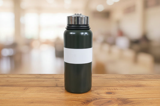 Black water bottle with silver cap held by a hand against a cluttered background