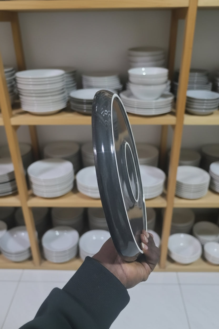 Person holding a dinner plate in a cluttered workshop with shelves of tools and equipment.