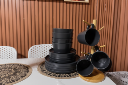 Set of black ceramic pots on a table with a wooden wall and framed pictures in the background.