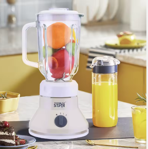 Blender with fruits, a glass of juice, and a slice of cake on a kitchen counter.