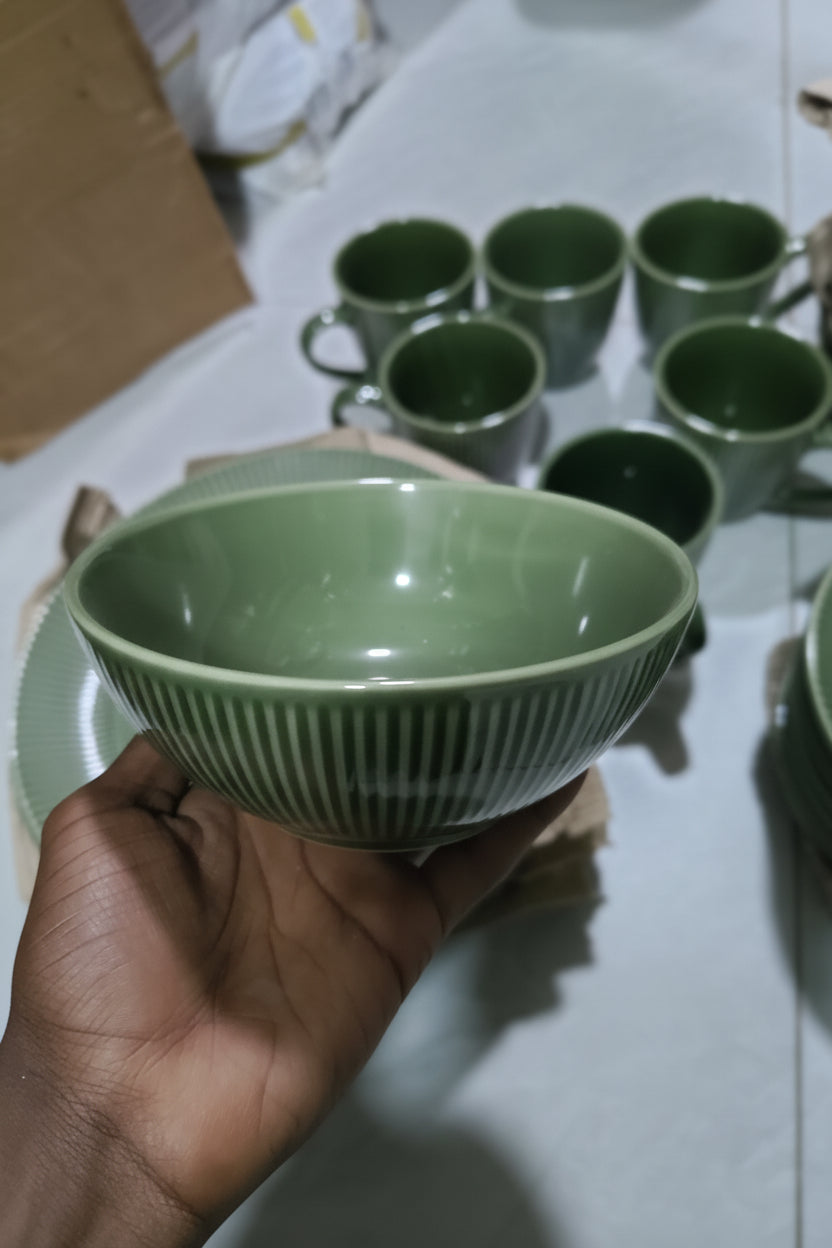 Green ceramic bowl held by a hand with more bowls stacked in the background.