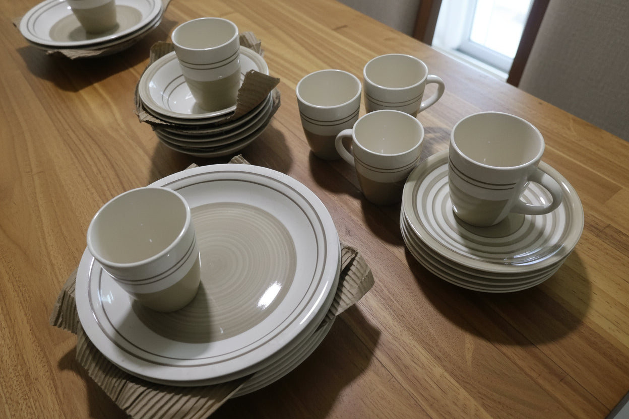 Set of ceramic dishes including cups and plates on a tiled floor.