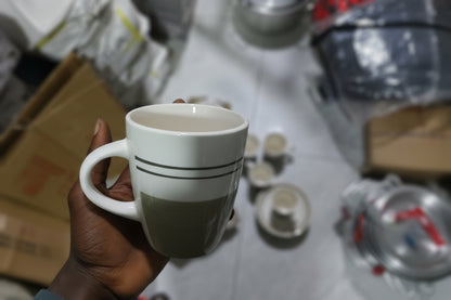 Hand holding a white mug with a gray lid in a cluttered room.
