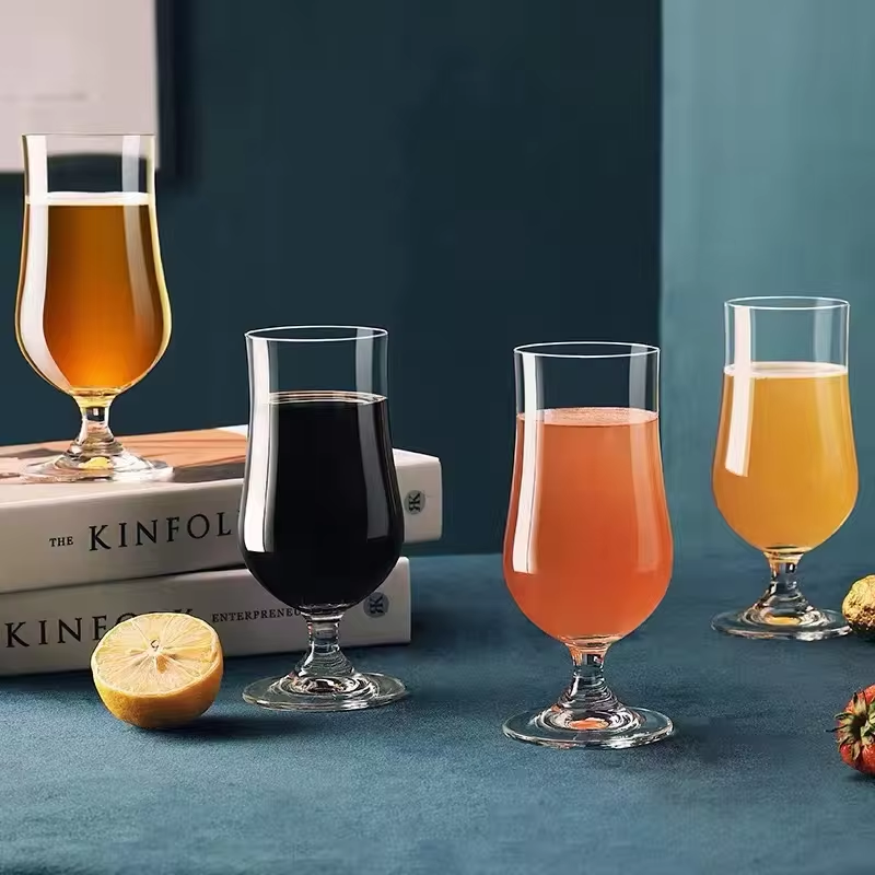 Four glasses with different colored drinks on a blue surface with books and a lemon.