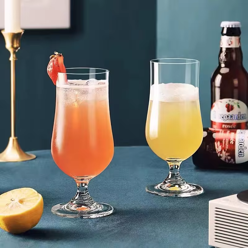 Two glasses of drinks on a table with a bottle and lemon in the background.