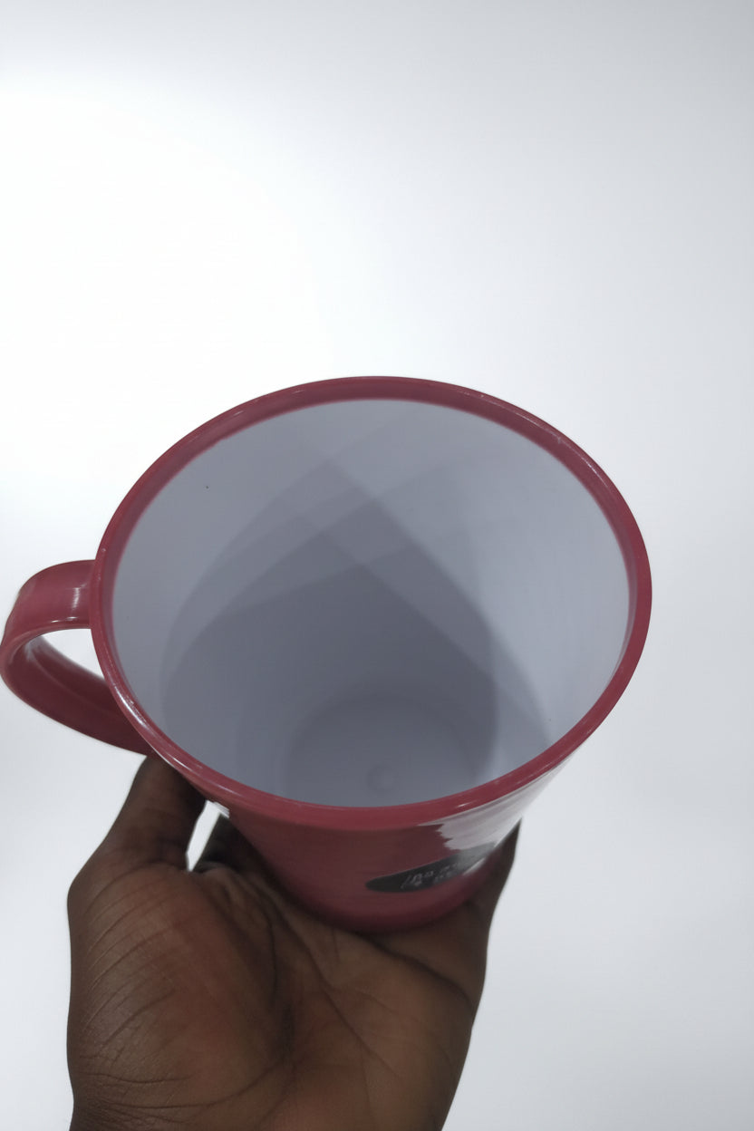 Hand holding a pink container with a white lid against a background of stacked glass items.