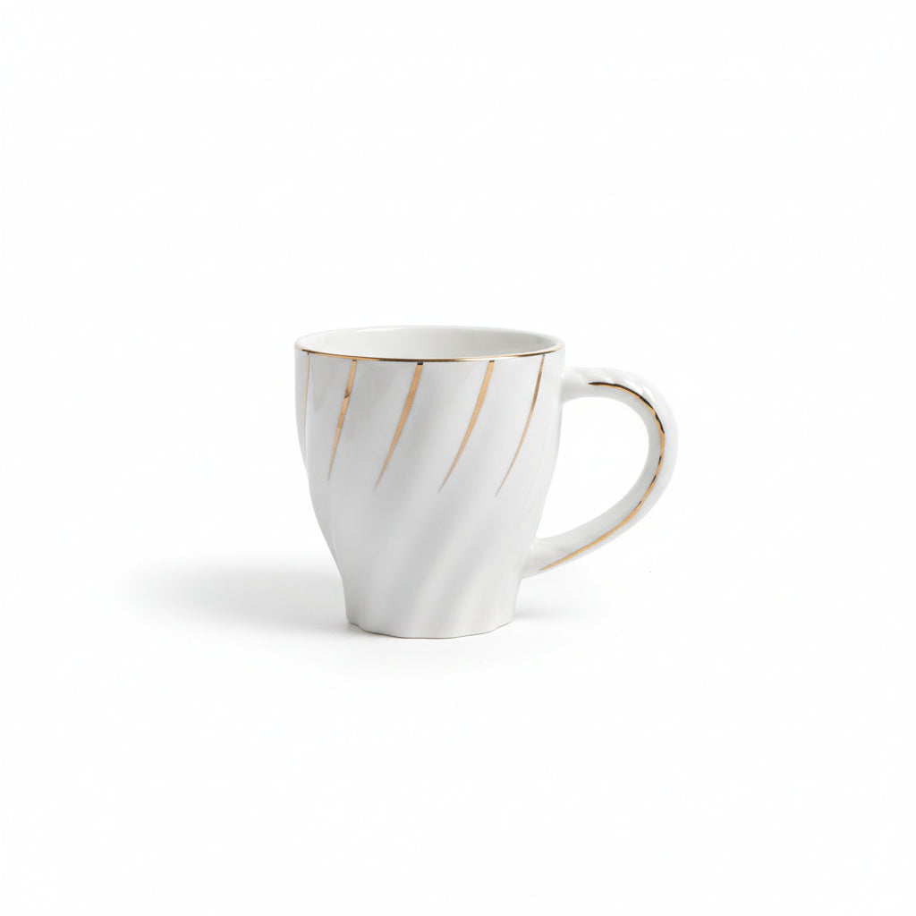 White ceramic mug with gold accents held by a hand against a blurred background of more mugs and dishes.