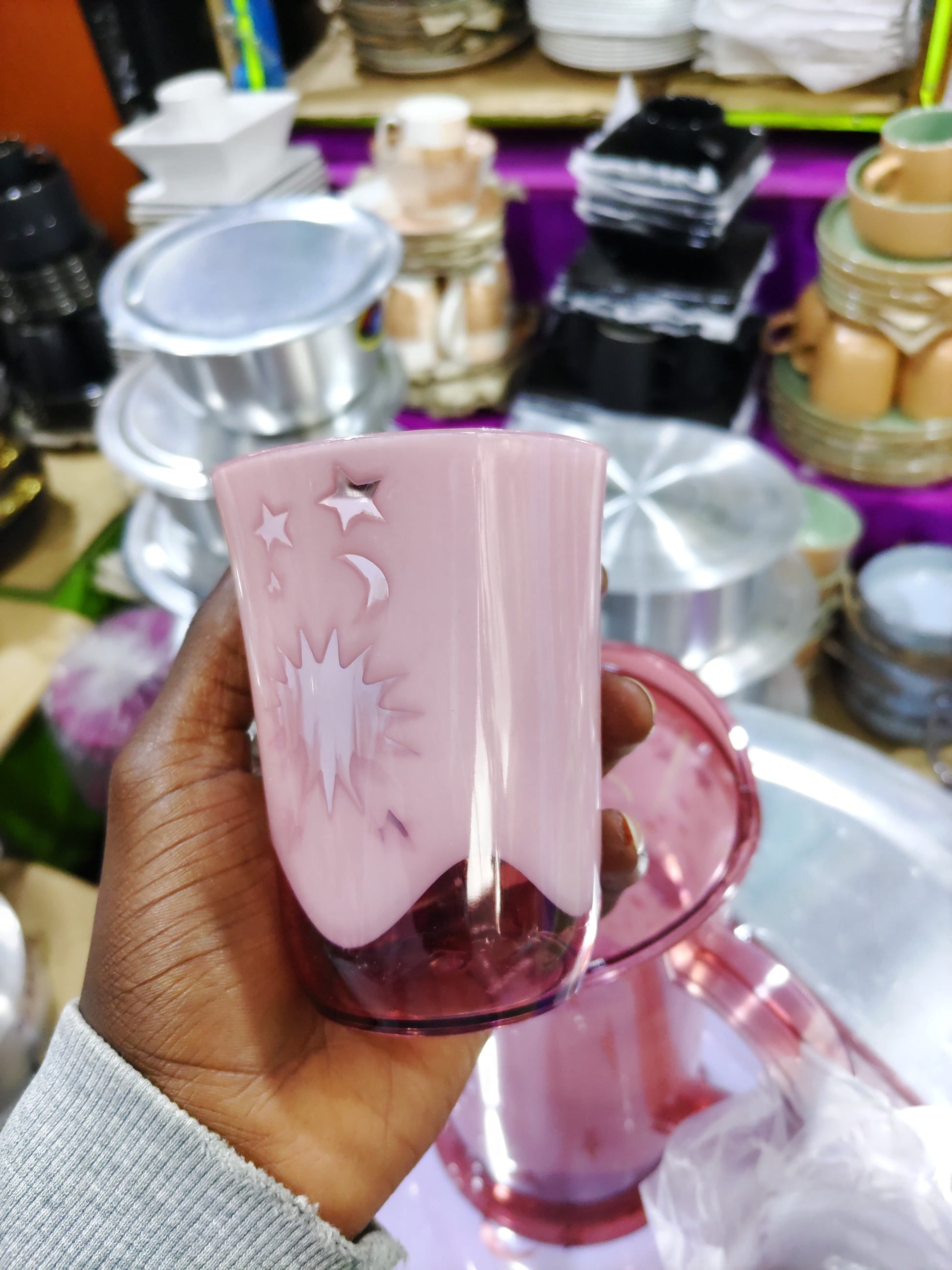 Hand holding a pink container with decorative elements against a cluttered background