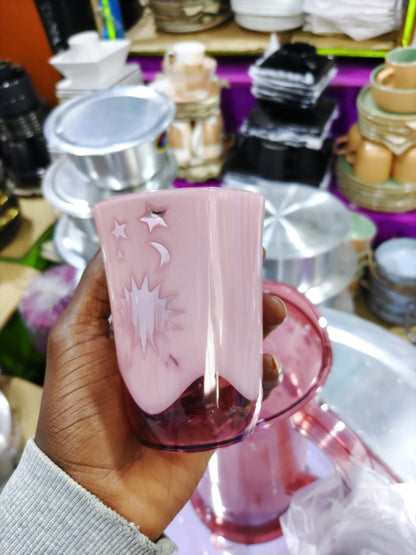 Hand holding a pink container with decorative elements against a cluttered background
