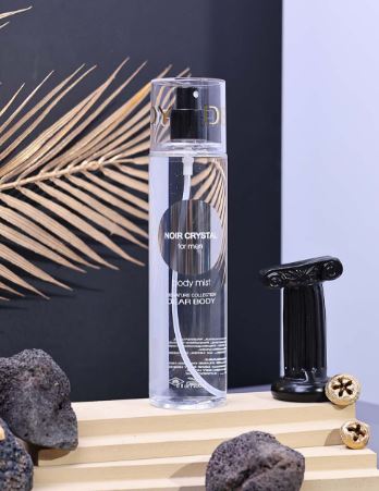 Clear spray bottle labeled 'Noir Crystal' on a wooden surface with decorative elements.