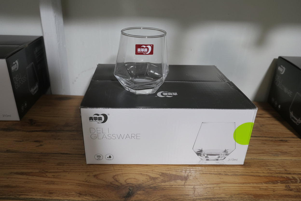 Clear glass mug leaning against a Cuisinart glassware box on a white surface.