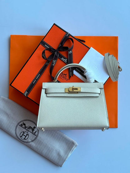 Light gray handbag with gold hardware on an orange Hermes box, with a gray cloth and black logo card.