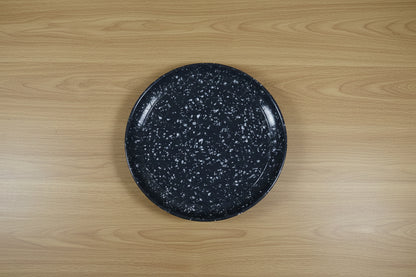 Black speckled frying pan held by a person in a cluttered store setting