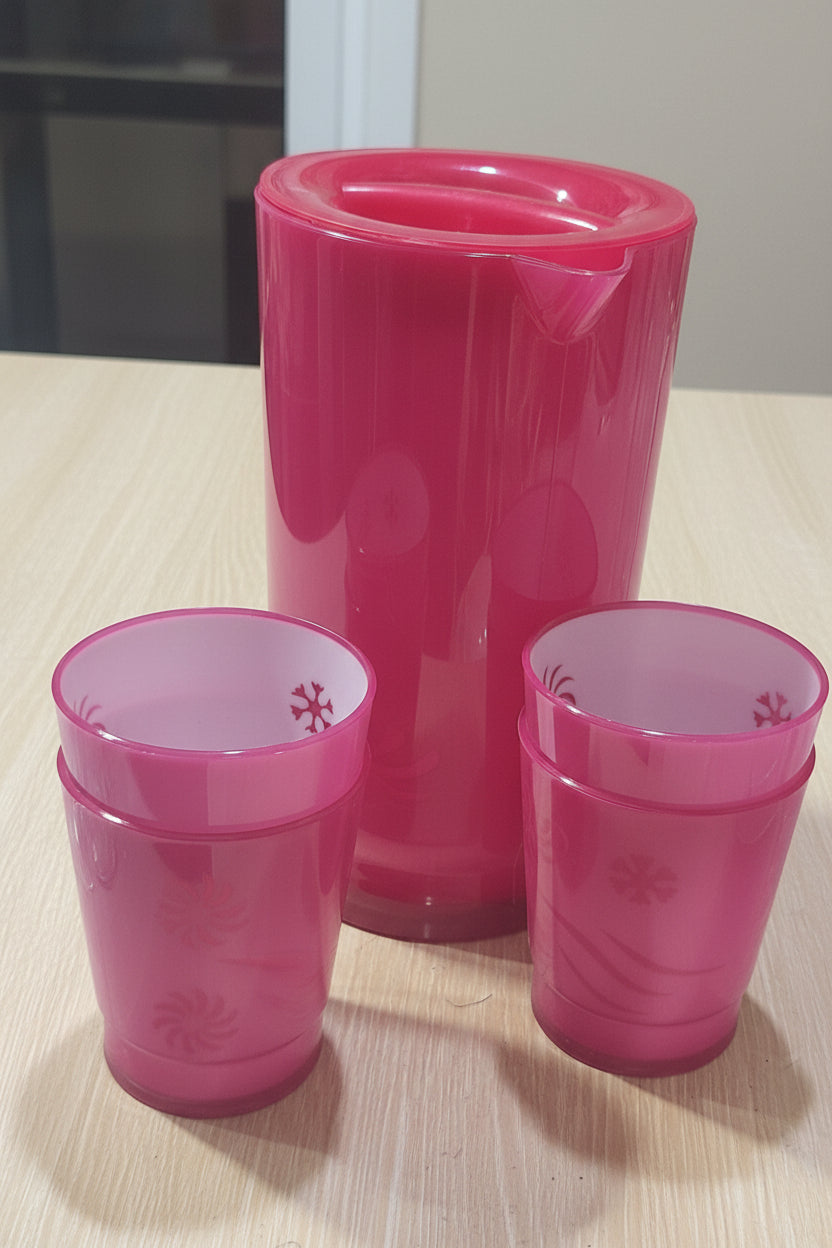 Pink tumblers and a clear glass pitcher on a wooden surface.