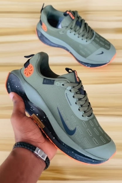 Two green running shoes with orange accents on a wooden floor.