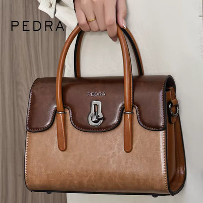 Brown handbag with wooden handle held by a hand, branded 'PEDRA'.