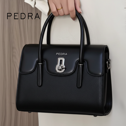 Black handbag with 'PEDRA' branding held by a hand against a neutral background