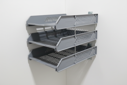 Three gray plastic drawers on a wooden surface with a white wall in the background.