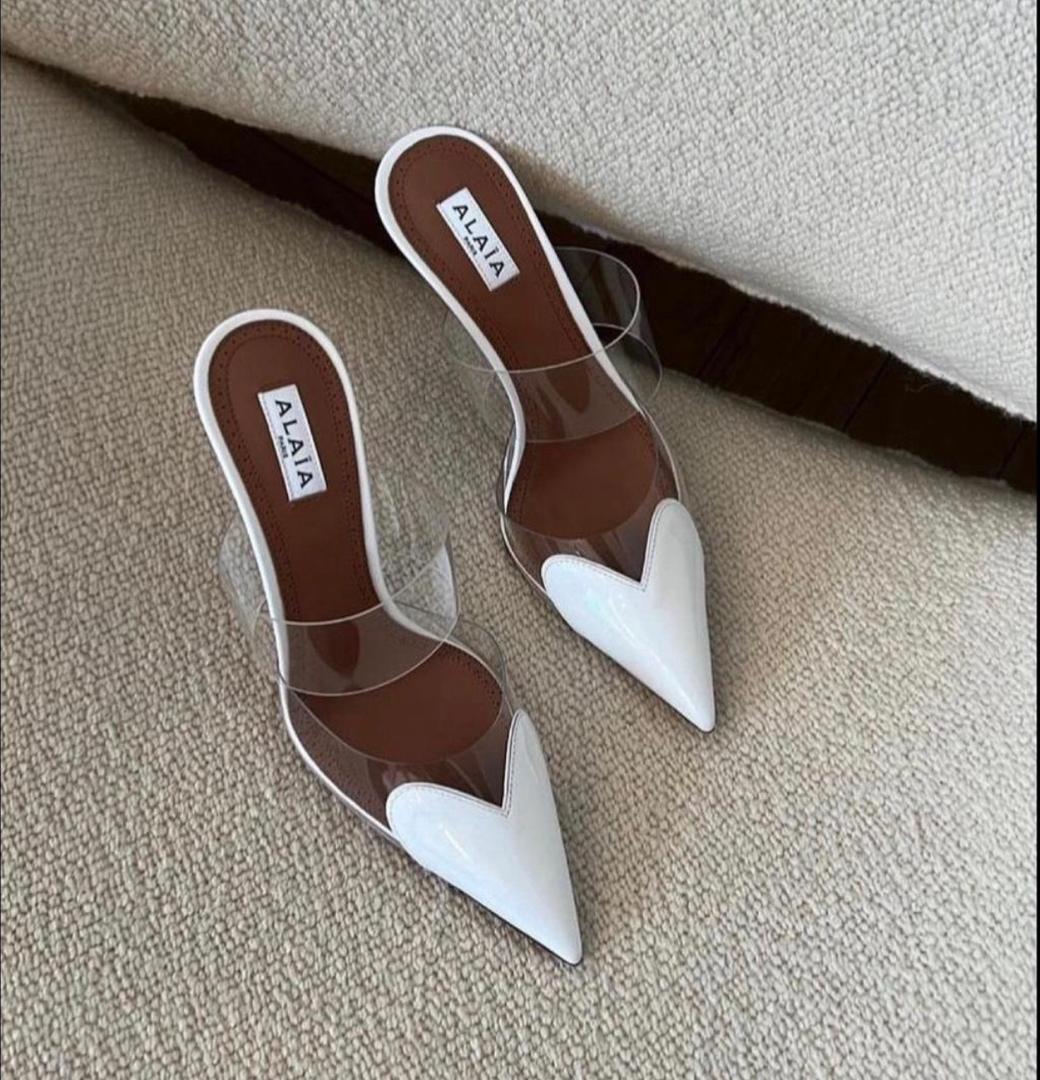 Pair of brown and white shoes with 'Alaia' branding on a beige surface.