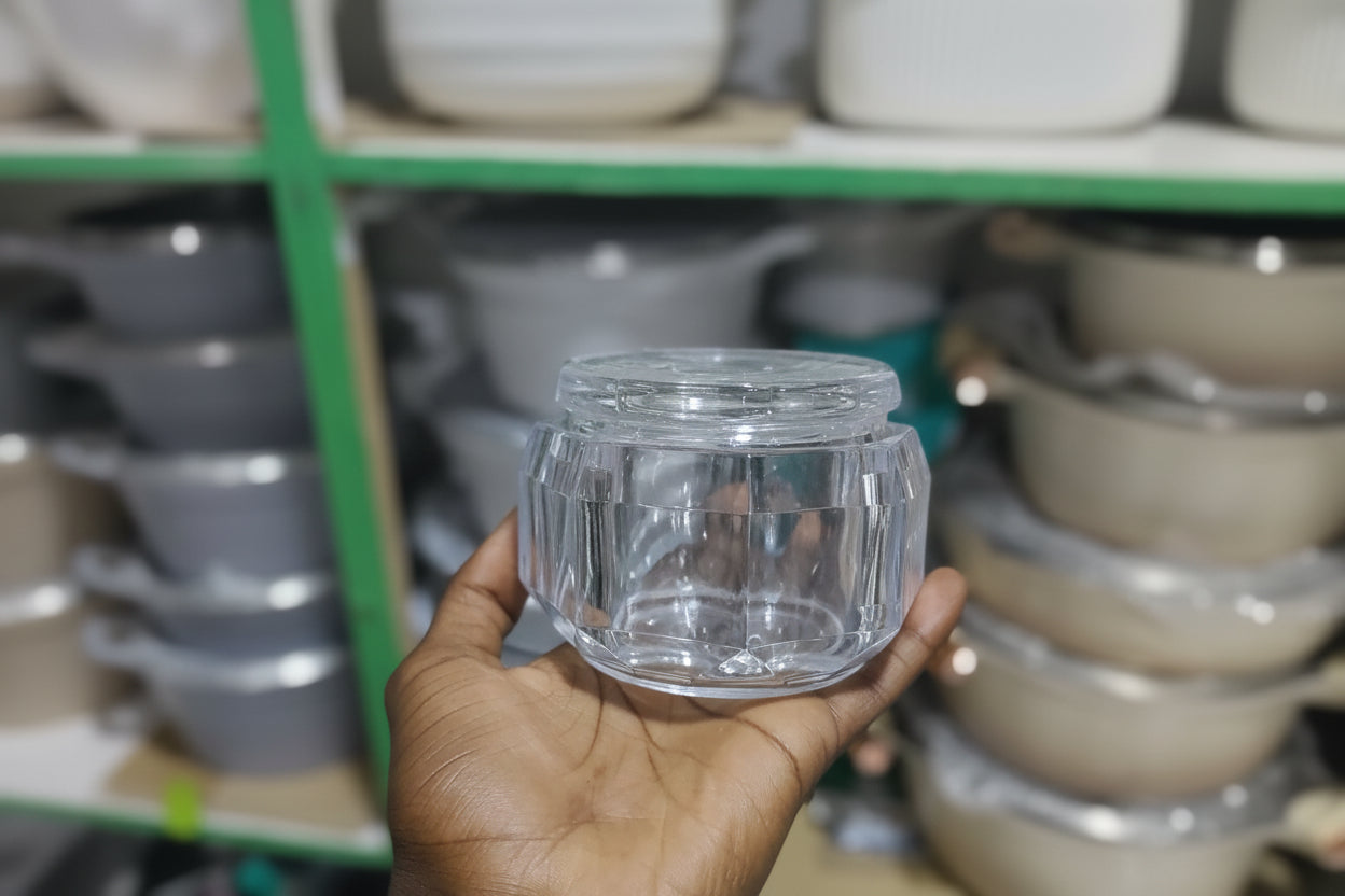 Hand holding a clear glass container with a blurred background of industrial equipment.